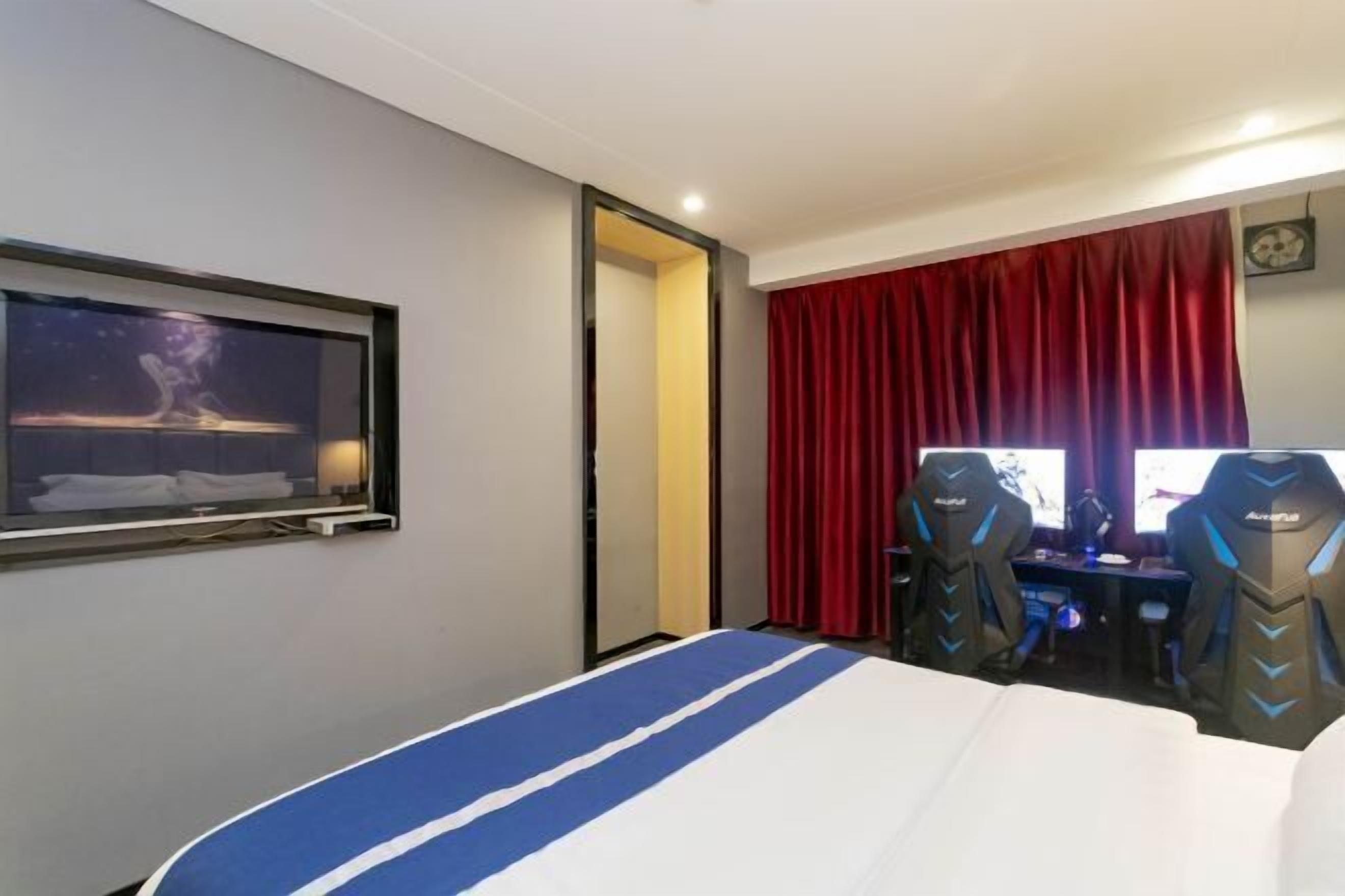 Une chambre d’hôtel avec un lit, un bureau, deux fauteuils de jeu, une télévision et un rideau rouge.