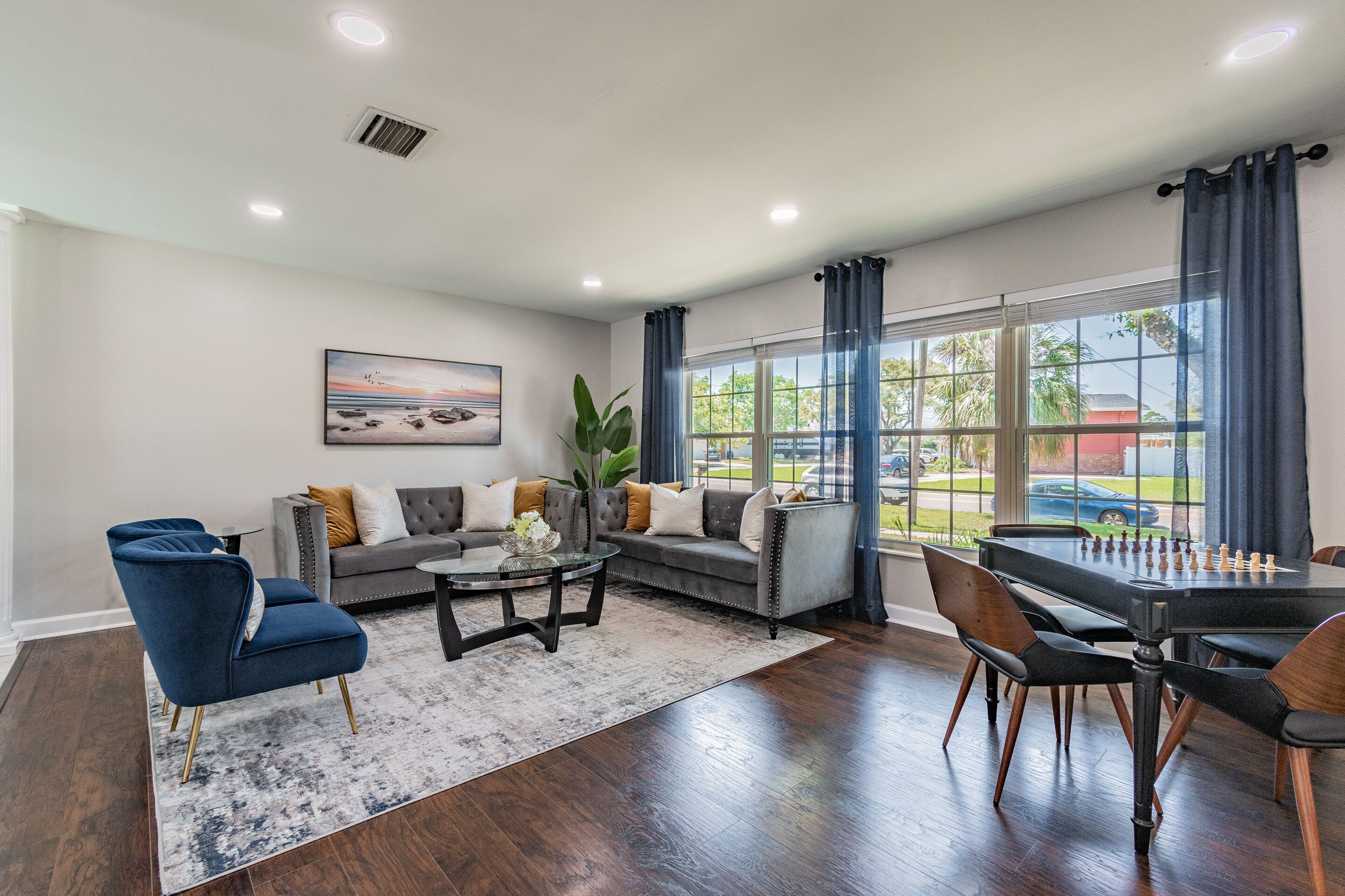 A spacious living room with a grey sofa, blue armchairs, a coffee table, and a dining table with chairs.