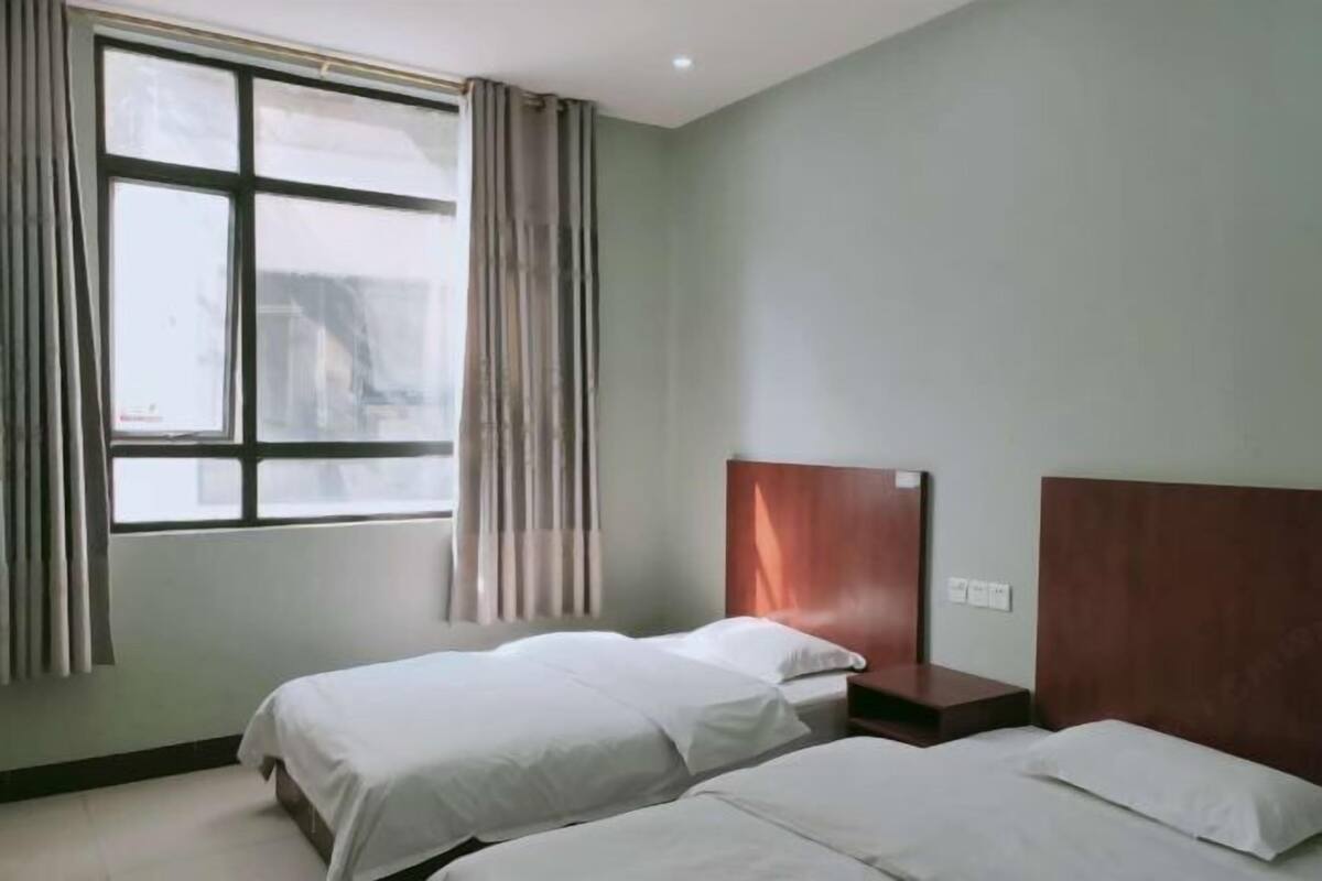 Une chambre d’hôtel avec deux lits, une fenêtre avec des rideaux et une tête de lit en bois.