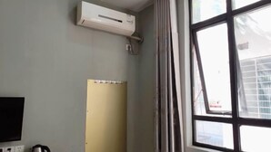 Een kamer met een groot raam, een airconditioningapparaat aan de muur en een flatscreen televisie.