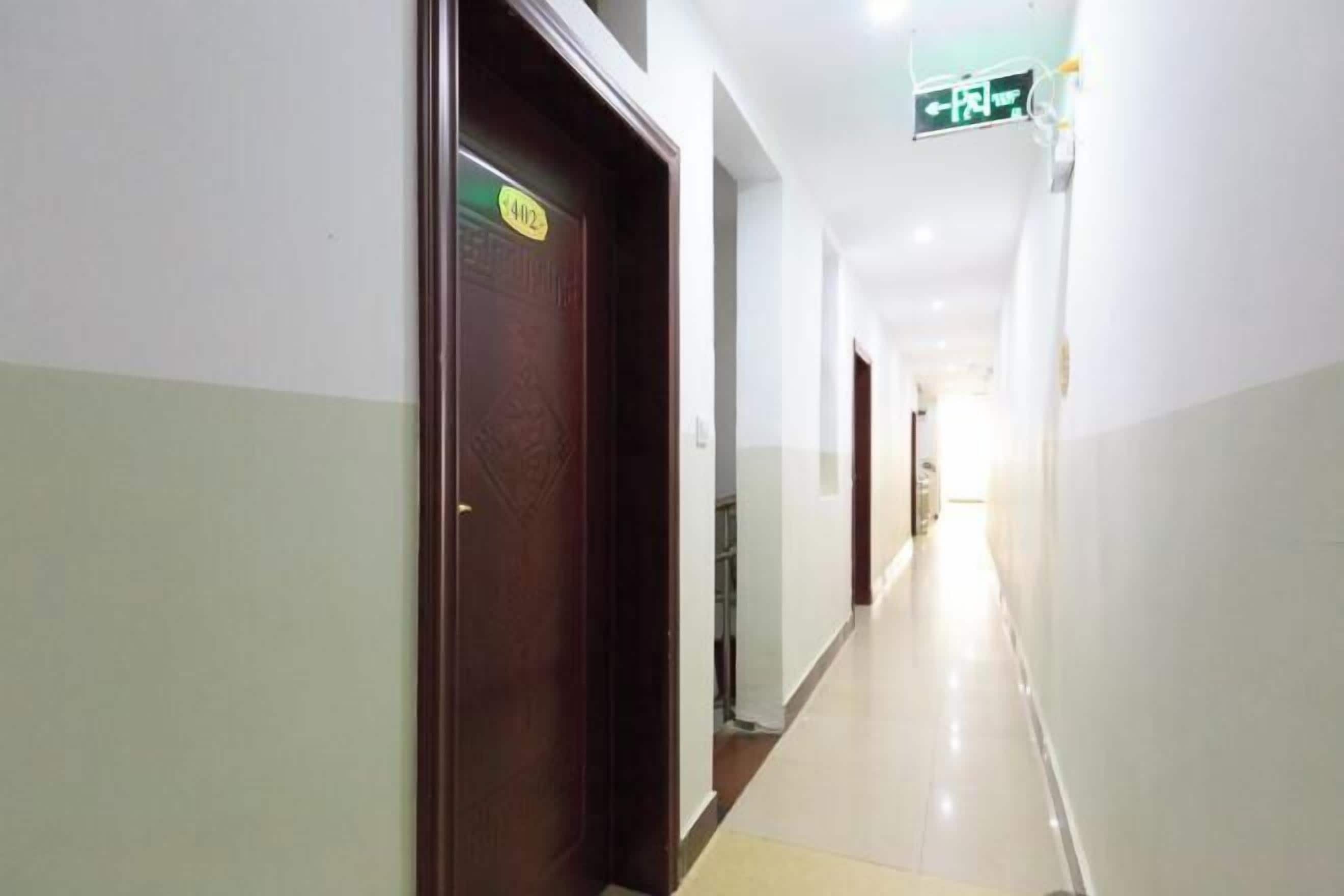 A long, narrow hallway with a wooden door on the left and a sign above it.
