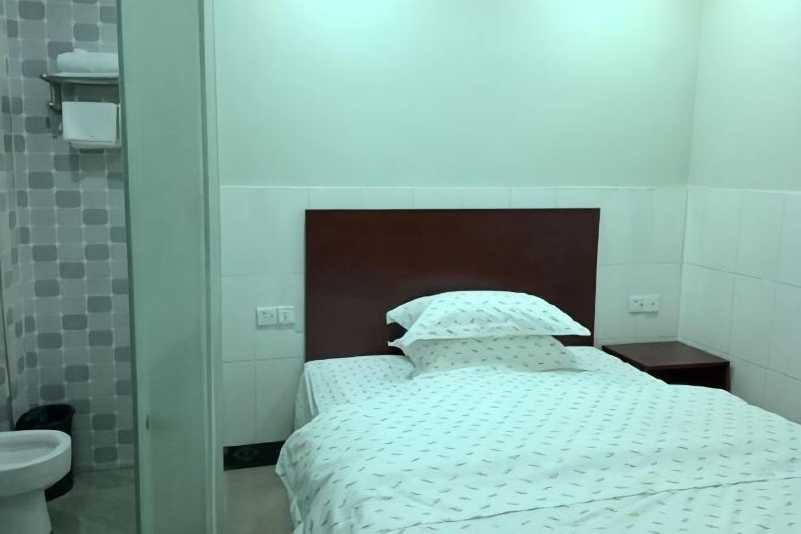 A small, clean room with a single bed, a nightstand, a toilet, and a shower area.