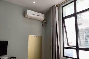Een kamer met een groot raam, een airconditioning, een flatscreen televisie en een waterkoker op het aanrecht.