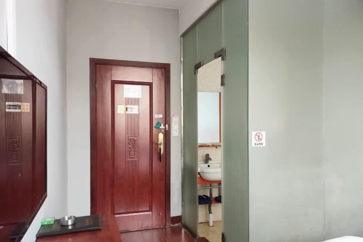 A hotel room with a wooden door, a green wall, and a visible bathroom with a sink and towel rack.