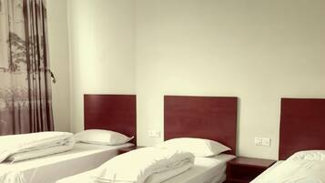 A hotel room with three single beds, each with a wooden headboard and white bedding.