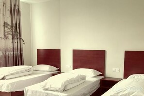 A hotel room with three single beds, each with a wooden headboard and white bedding.