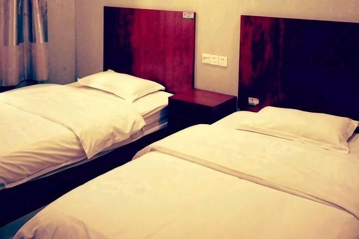 Deux lits simples avec du linge de lit blanc, des têtes de lit en bois et un mur d’accent rouge.