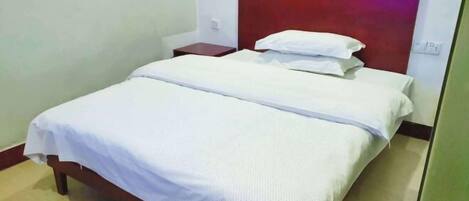 Una cama individual con estructura de madera, ropa de cama blanca y cabecera roja.