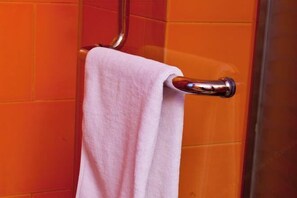 A bathroom with orange tiles and a chrome towel rack holding a white towel.