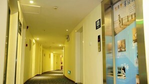 A hotel corridor with a patterned carpet, framed pictures on the walls, and a blue informational poster on the right. - 7 Days Holiday Hotel (Guiyang Gaicha Avenue Zhongshan Middle Road) (Guiyang)