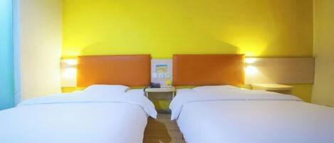 A hotel room with two beds, a wooden floor, a nightstand with a lamp, and a wall-mounted phone.