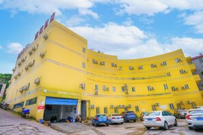 A yellow multi-story building with a blue garage door, several parked cars, and a clear sky. - 7 Days Holiday Hotel (Guiyang Gaicha Avenue Zhongshan Middle Road) (Guiyang)