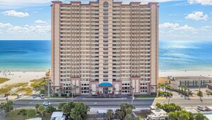 Un hotel de gran altura con varios balcones, una entrada central y vista a la playa y el océano.