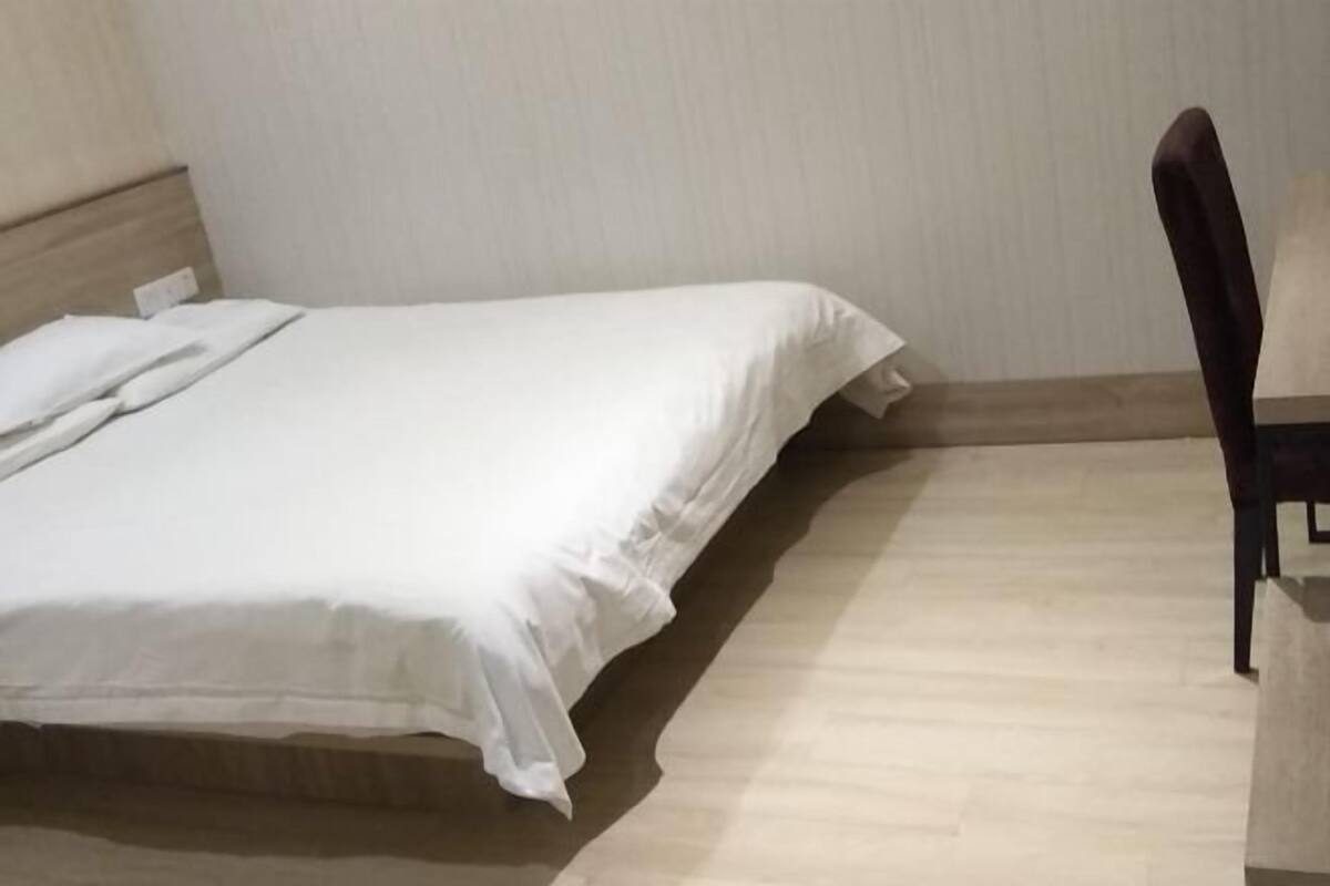 Ein Einzelbett mit Holz-Kopfteil, ein Stuhl und ein heller Holzboden.