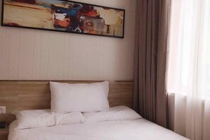 A hotel room with a bed, a headboard, a painting on the wall, and curtains on the window. - Pebble Motel (Jiusan Road Bus Station, Lvshun) (Dalian)