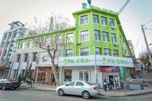 A multi-story building with a green facade, a storefront with signage, and a parked car on the street. - Pebble Motel (Jiusan Road Bus Station, Lvshun) (Dalian)