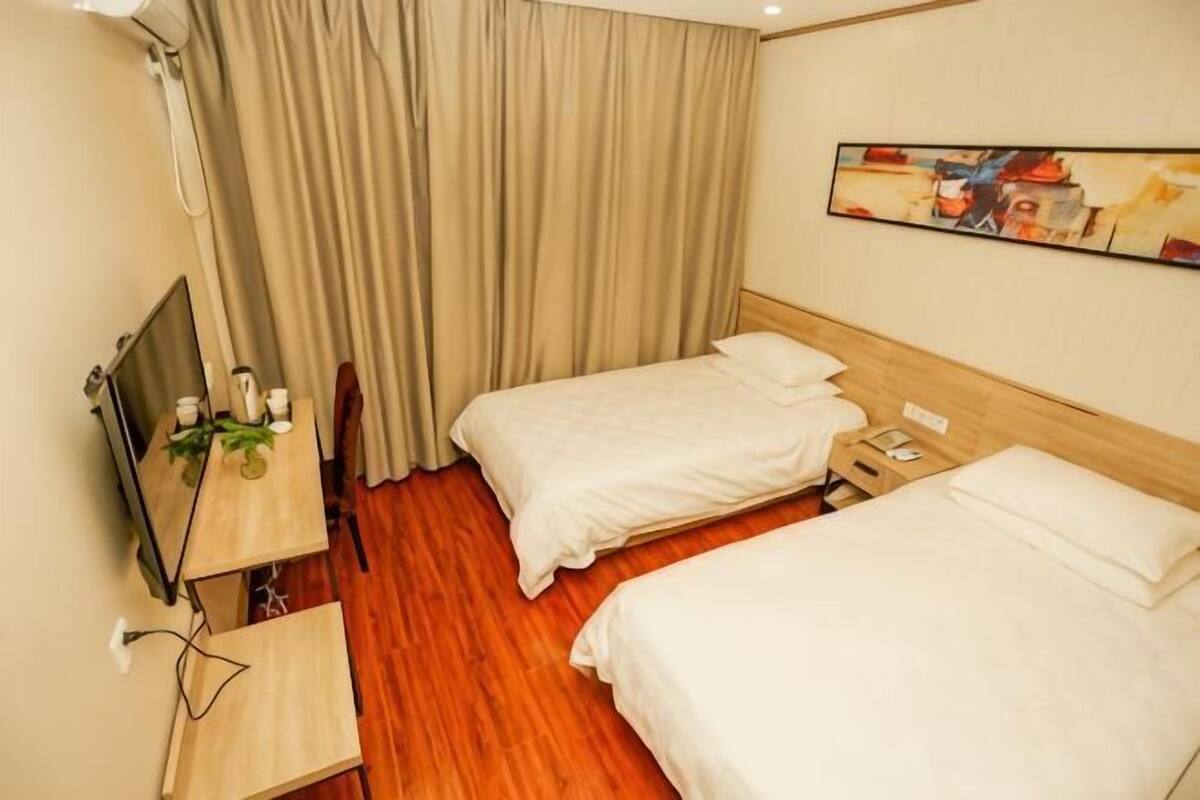 Ein Hotelzimmer mit zwei Betten, einem Schreibtisch mit Stuhl, einem Fernseher und einem Vorhang.
