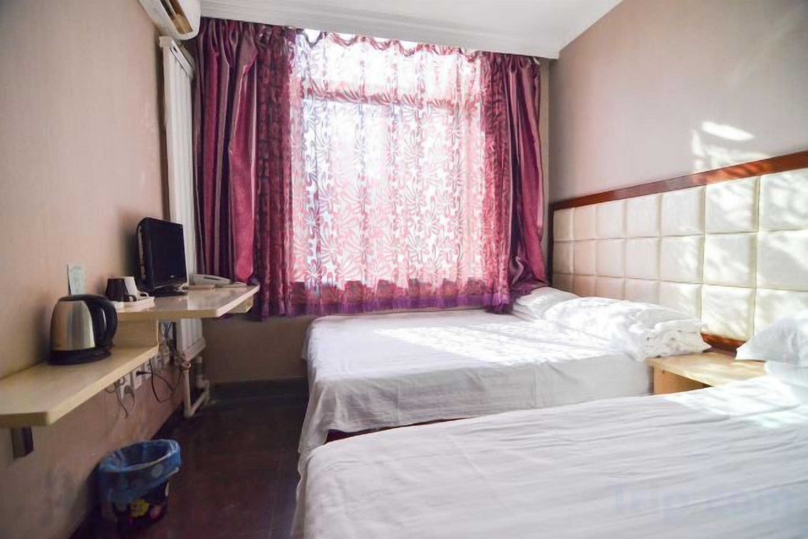 Una habitación de hotel con dos camas, un escritorio con computadora y un ventanal con cortinas.
