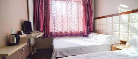 Una habitación de hotel con dos camas, un escritorio con computadora y un ventanal con cortinas.