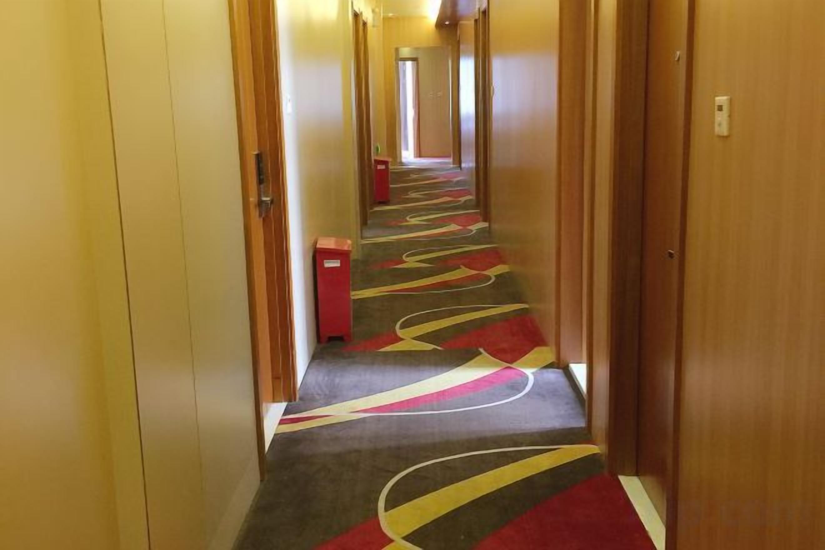 A hotel corridor with carpeted flooring and wooden doors.