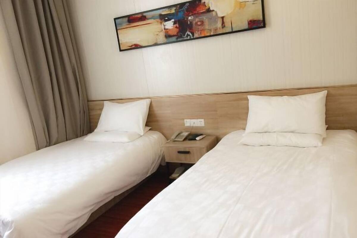 Ein Hotelzimmer mit zwei Einzelbetten, einem Holzkopfteil, einem Nachttisch mit Telefon und einem Bild an der Wand.