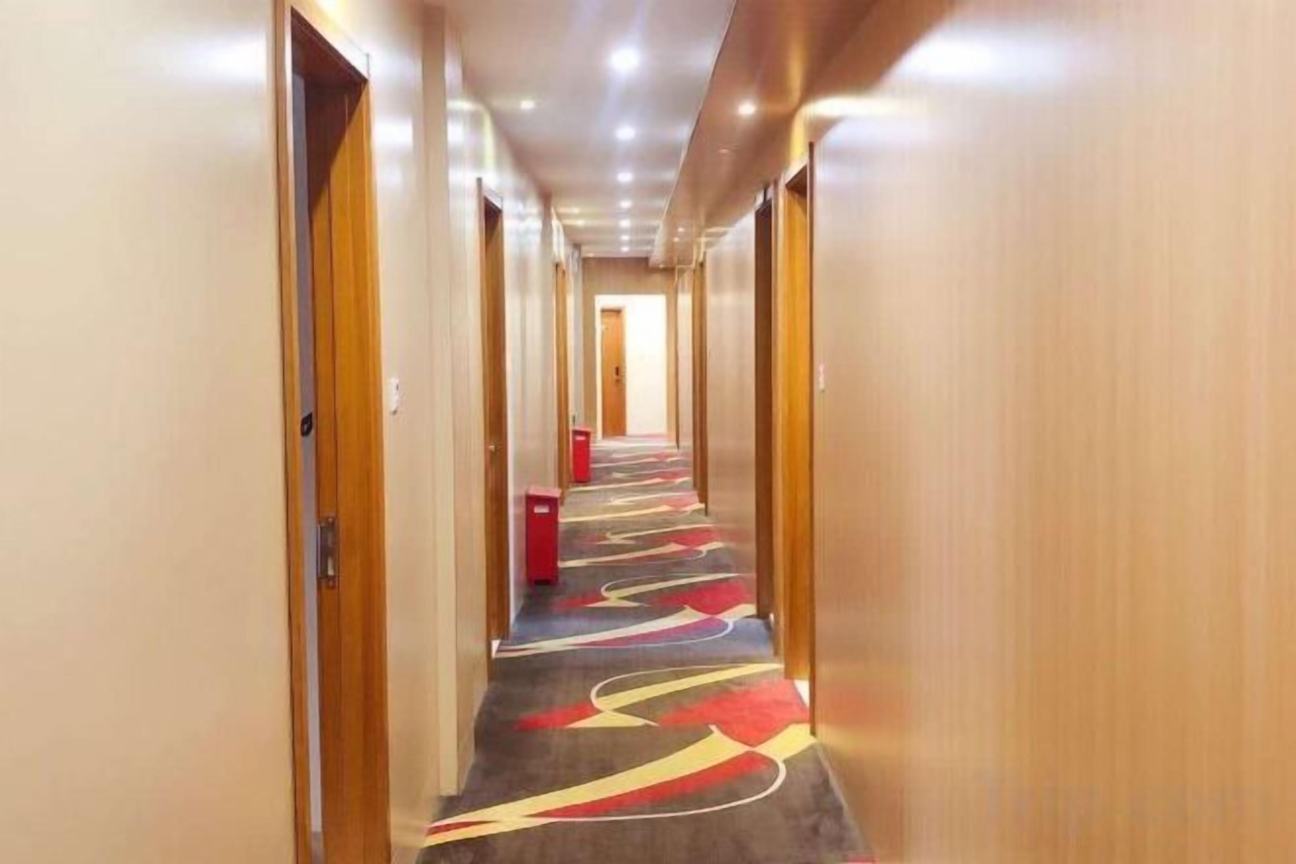 Ein Hotelkorridor mit Türen auf beiden Seiten, einem gemusterten Teppich und einem roten Gegenstand am Boden.
