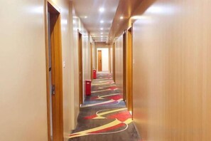 A hotel corridor with doors on both sides, a patterned carpet, and a red object on the floor. - Pebble Motel (Jiusan Road Bus Station, Lvshun) (Dalian)