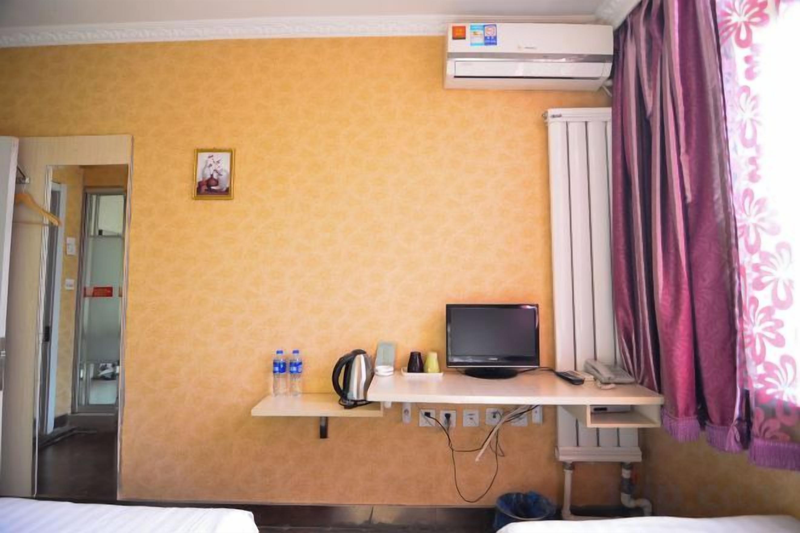 Una habitación de hotel con una cama, un escritorio con televisor, un radiador y una puerta que da a otra habitación.
