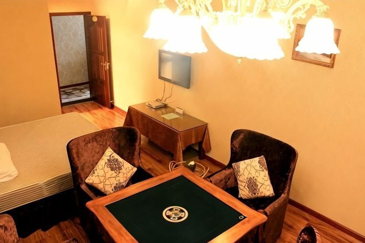 Une chambre d’hôtel comprenant un lit, deux fauteuils, une petite table, un téléviseur et un lustre.