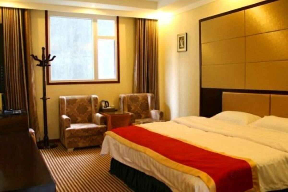 Habitación de hotel con cama, dos sillones, una mesita con una taza, perchero y ventana con cortinas.