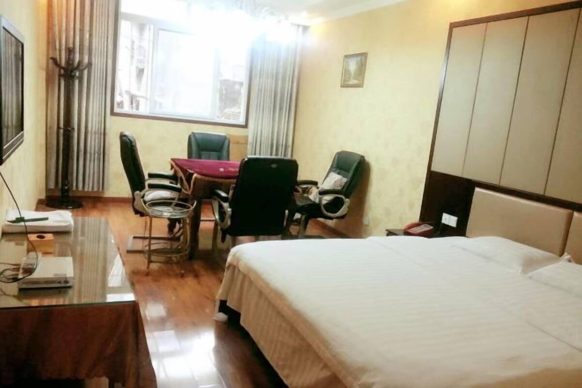Habitación de hotel con una cama, un escritorio con silla, una mesa con silla, un televisor y una ventana con cortinas.