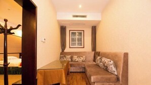 A room with a wooden floor, a sofa with floral cushions, a small table, and a window with curtains.