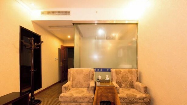 A hotel room with a sofa, a small table, a coat rack, and a door.