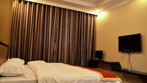A hotel room with a bed, curtains, a television, and a speaker.