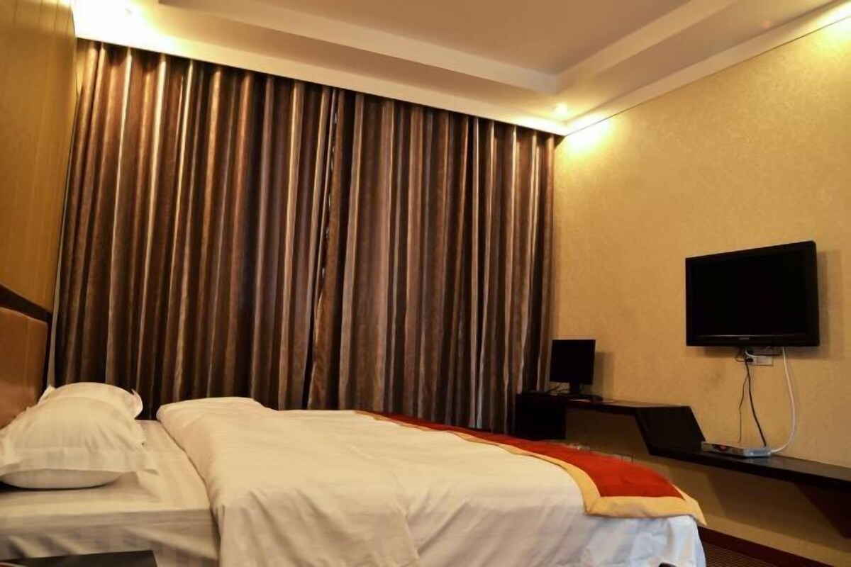 Quarto de hotel com cama, cortinas, televisão e um alto-falante.