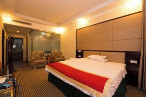 A hotel room with a large bed, a headboard, a seating area with chairs, and a mirror.