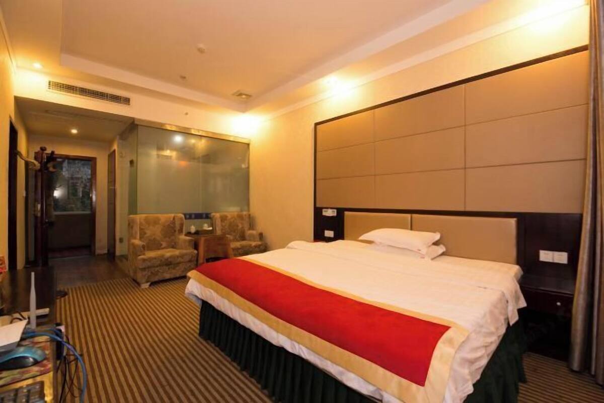 Habitación de hotel con una cama grande, una zona de estar con sillas, un escritorio y un ventanal amplio.