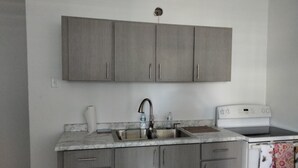 Una cocina con gabinetes grises, un lavamanos de acero inoxidable y una estufa blanca.