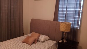 Una cama con cabecera, dos almohadas, una lámpara de noche y una mesita de noche con un teléfono.