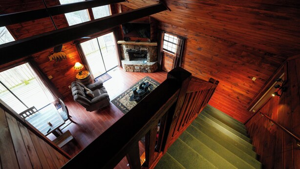 Interior de una cabaña de madera con chimenea, comedor y escalera.