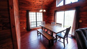 Interior de una cabaña de madera con una mesa de comedor, bancos y ventanas amplias.