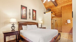 Une chambre à coucher avec un lit en bois, deux tables de chevet avec des lampes, une tête de lit en bois et des œuvres d’art florales encadrées accrochées au mur.