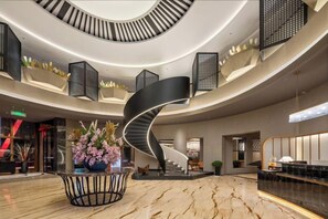Een moderne hotellobby met een marmeren vloer, een centrale spiraaltrap en een receptiebalie.