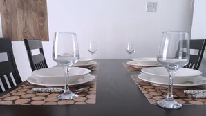 A dining table with four chairs, each with a white plate and a clear glass.