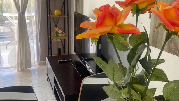 A room with a wooden coffee table, a vase with roses, a clock on the wall, and a piano in the background.