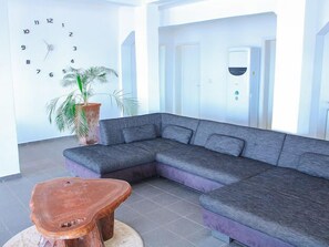 Una sala de estar moderna con un sofá seccional gris, una mesa de centro de madera, un reloj de pared grande y una planta en maceta.