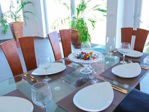 Mesa de comedor preparada para cuatro personas, con copas de cristal transparente, sillas de madera y un centro de mesa con caramelos de colores.