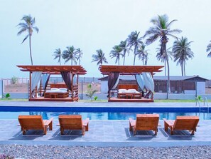 A poolside area with wooden loungers and two wooden beds with canopies. - Impeccable 3-Bed House in Prampram Accra (Prampram Accra)