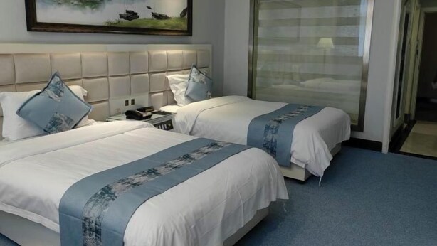 A hotel room with two beds, a headboard, a painting, and a sliding door.
