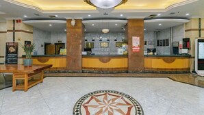 A hotel reception area with a marble floor, a central chandelier, and a reception desk.